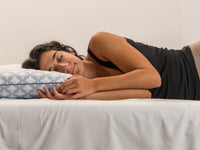 Woman sleeping on a bed with a Luxury cooling pillow, wearing a black tank top.